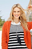 A young blonde woman outside wearing a black-and-white stripped jumper and an orange knitted cardigan