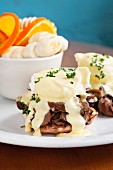 An English muffin topped with a poached egg, mushrooms and Hollandaise sauce served with oranges and bananas