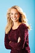 A young blonde woman with her arms folded wearing a burgundy knitted jumper