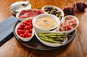 Hummus dip with ham, salami, olives and vegetables in bowls