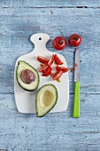 A halved avocado and tomatoes on a chopping board