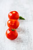 A row of three tomatoes with a leaf