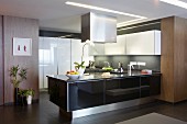 Designer kitchen in mixture of materials - counter with glossy black front below stainless steel extractor hood and white overhead cabinets on grey wall