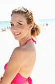 A young blonde woman on a beach wearing a pink bikini top