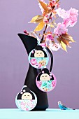 Hand-crafted, Japanese Kokeshi pendants on jug holding branches of cherry blossom