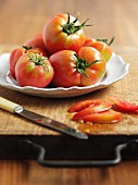 Mehrere Tomaten auf weißem Teller und geschnittene Tomate auf Holzbrett