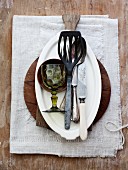 Various kitchen utensils, crockery, cutlery and a wine glass on a linen cloth