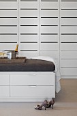 Ladies' shoes and half-height chest of drawers with upholstered top in front of white fitted cupboards with slotted doors