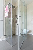 A floor-level, tiled shower cubicle with a rain shower and a hand-held shower head with a glass partition wall in a designer bathroom