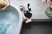A partially visible bathtub next to an old-fashioned black telephone on a platform