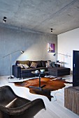 Bistro table on animal-skin rug, black corner couch against exposed concrete wall and retro shell chair in foreground