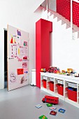 Spielecke, offenes Sideboard mit roten Aufbewahrungskörben, im Hintergrund Tür mit beklebten Kinderzeichnungen
