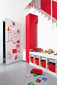 Play area; open-fronted sideboard with red storage boxes and door covered in child's drawings