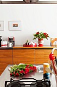 Kitchen island with red tulips on stainless steel worksurface and pale wood sideboard