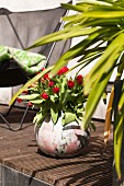 Red tulips in spherical vase on wooden terrace floor