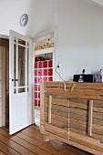 Rustic sideboard with wooden board front next to open door with view of cabinet with small, red doors in hallway