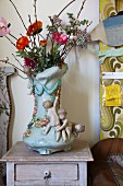 Eclectic furniture and accessories; china vase decorated with garlands and children next to wall panel with 70s floral pattern