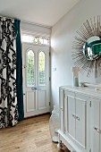 Sunburst mirror above vintage cabinet, front door with stained glass transom light and curtain with classic pattern