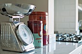 Retro kitchen scales next to Chinese tea caddies on marble kitchen counter in country-house interior