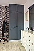 Bedroom with white dressing table and black fitted wardrobe against floral wallpaper