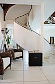 Open-plan interior; wicker armchairs with white seat cushions, elegant white spiral staircase with solid balustrade