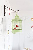 Metal bird ornaments in green vintage birdcage hanging from metal wall bracket