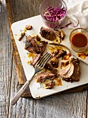 Pulled pork on a ceramic platter with forks, spicy sauce and pickled red cabbage