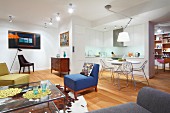 Colourful armchairs, glass coffee table, cowhide rug and wooden floor; dining area with wire chairs and open-plan kitchen in background