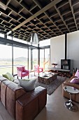 Leather sofa set and pink armchairs around block-style coffee table next to glass wall with view of landscape