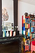 Painted plastic bottles used as flower vases on mantelpiece next to patchwork-style bookshelves