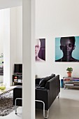 Modern, black leather couch behind pillar; large portraits on wall