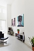 Living area with sideboards against wall below large portraits in loft apartment