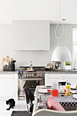 Set breakfast table below pendant lamp with pale lampshade and kitchen counter in background