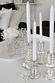 White candles in silver candlesticks and posy of rose and gypsophila