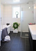 White bathroom with glazed shower cabinet, dark tiled floor and house plant below window in background