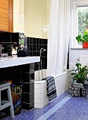 Tiles in mixture of colours and formats in bathroom; bathtub with shower curtain, masonry washstand and towels