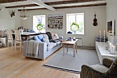 Dining area and seating area with sofa in open-plan interior with wooden walls and exposed ceiling beams