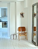 Minimalistisch möblierter Flurbereich mit Wandspiegel und Holzstuhl auf weißem Dielenboden