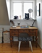Nostalgischer Schreibtisch mit Retrohocker vor Fenster mit Wählscheibentelefon