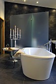 Pleasant bathroom with dark tiles, tray table and candelabra next to free-standing bathtub