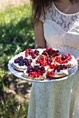 A little girl holding a plate of cherry and redcurrant tartlets