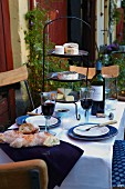 A table laid with red wine, baguette and a stand of cheese on a terrace
