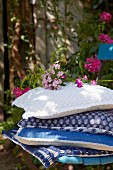 Gestapelte Kissen mit verschiedenen blauweissen Bezügen und Phlox-Blüten auf Stuhl im Garten