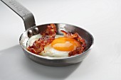 A fried egg with bacon in a pan