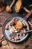Fresh forest mushrooms in an old pan with a fork on a wooden table (seen from above)
