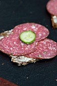 A slice of bread topped with salami and cucumber slices