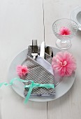 A place setting with a napkin folded as a cutlery bag decorated with paper carnations