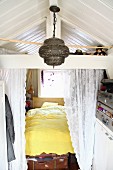 Eingebautes Bett mit Spitzenvorhang, davor orientalische Hängeleuchte und Aufbewahrung in Vintage Koffern