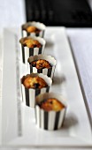Kleine Muffins in schwarz-weiss gestreiften Papierförmchen auf Kuchenplatte