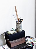 Can of drawing utensils on top of shoeboxes and painter's palettes on shelf